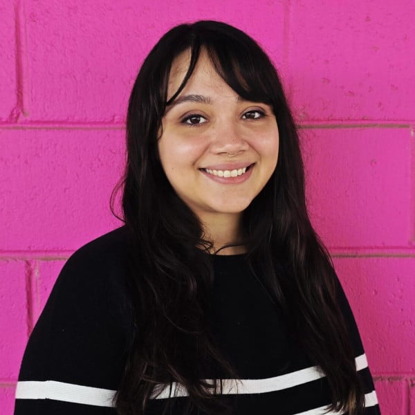 This is a head shot of a woman smiling with a pink brick background.